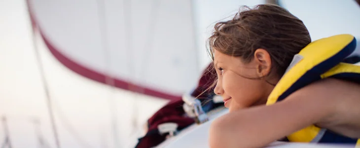 One girl on sailboat enjoying at summer and having a fun. He wears a safety west and looking at distance